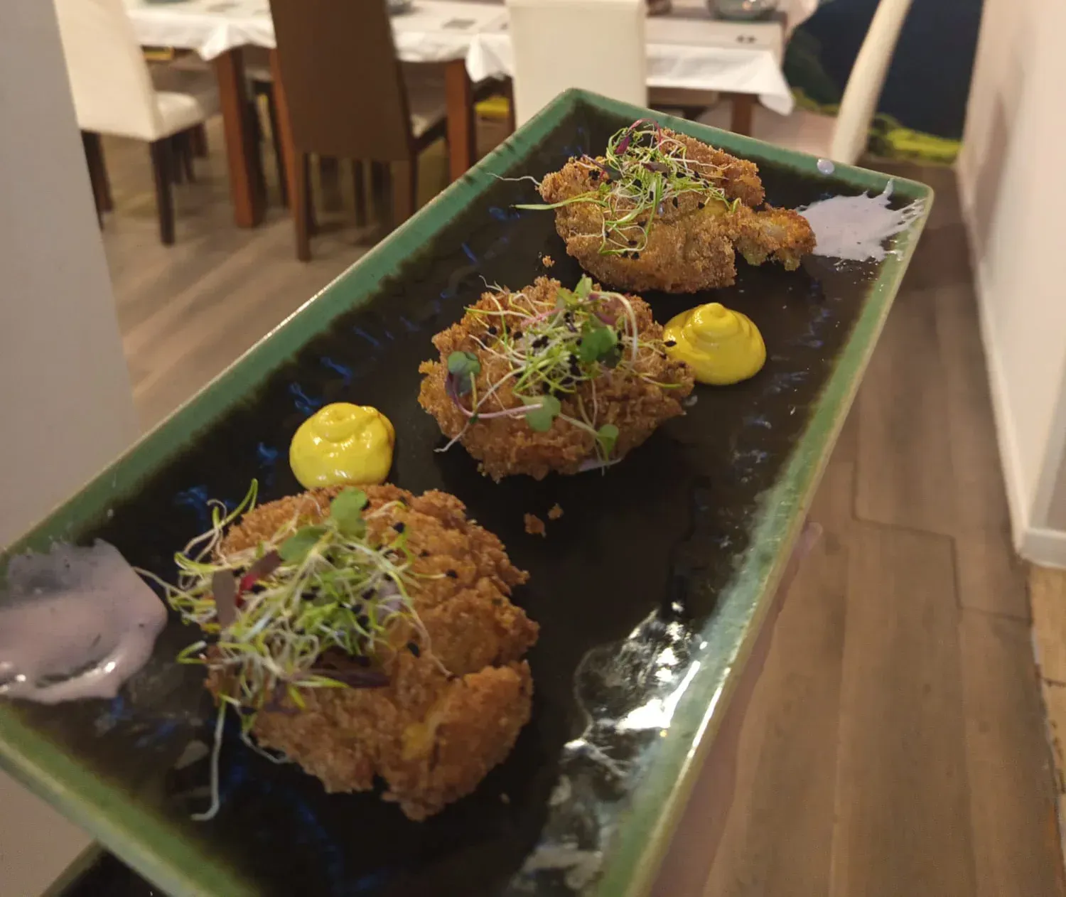 Tres porciones de comida frita con brotes, servidas en un plato rectangular negro con salsas.