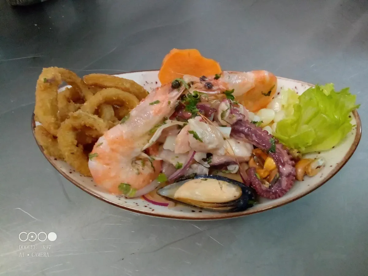 Ceviche de mariscos con calamares fritos, langostinos, mejillones y guarniciones en plato.