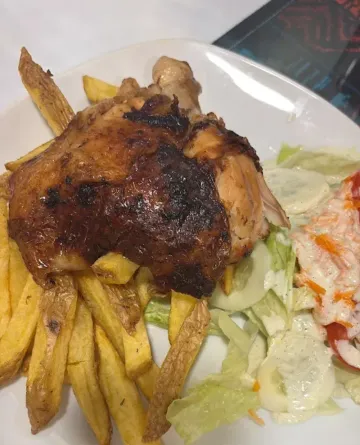 Cuarto de pollo asado con patatas fritas y ensalada en un plato blanco.