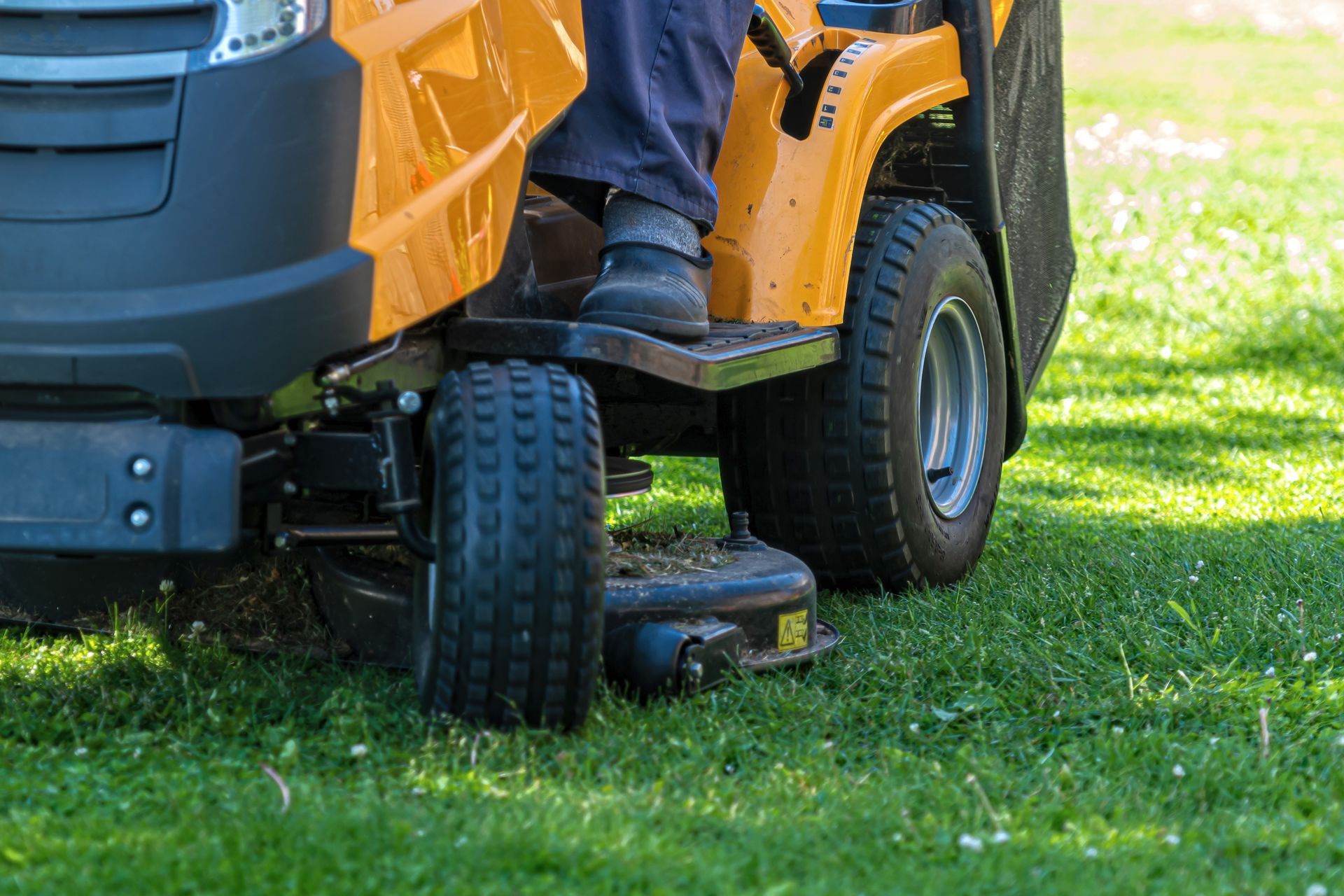 Tondeuse à gazon autoportée jaune sur l'herbe, avec le pied d'une personne sur le repose-pieds.