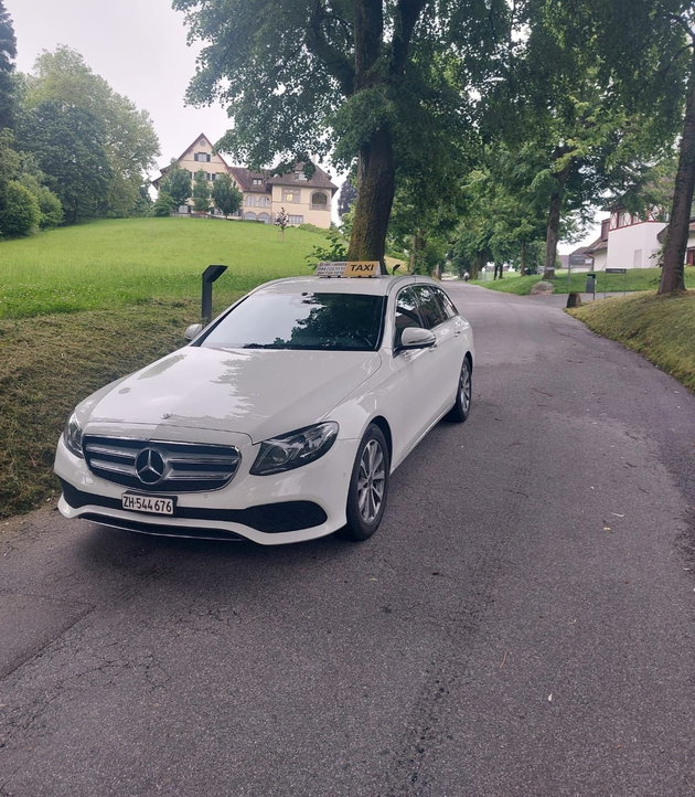 Ein weisses BMW-Taxi parkte in der Abenddämmerung an einer Strasse in der Nähe einer Grünfläche und Bäumen.