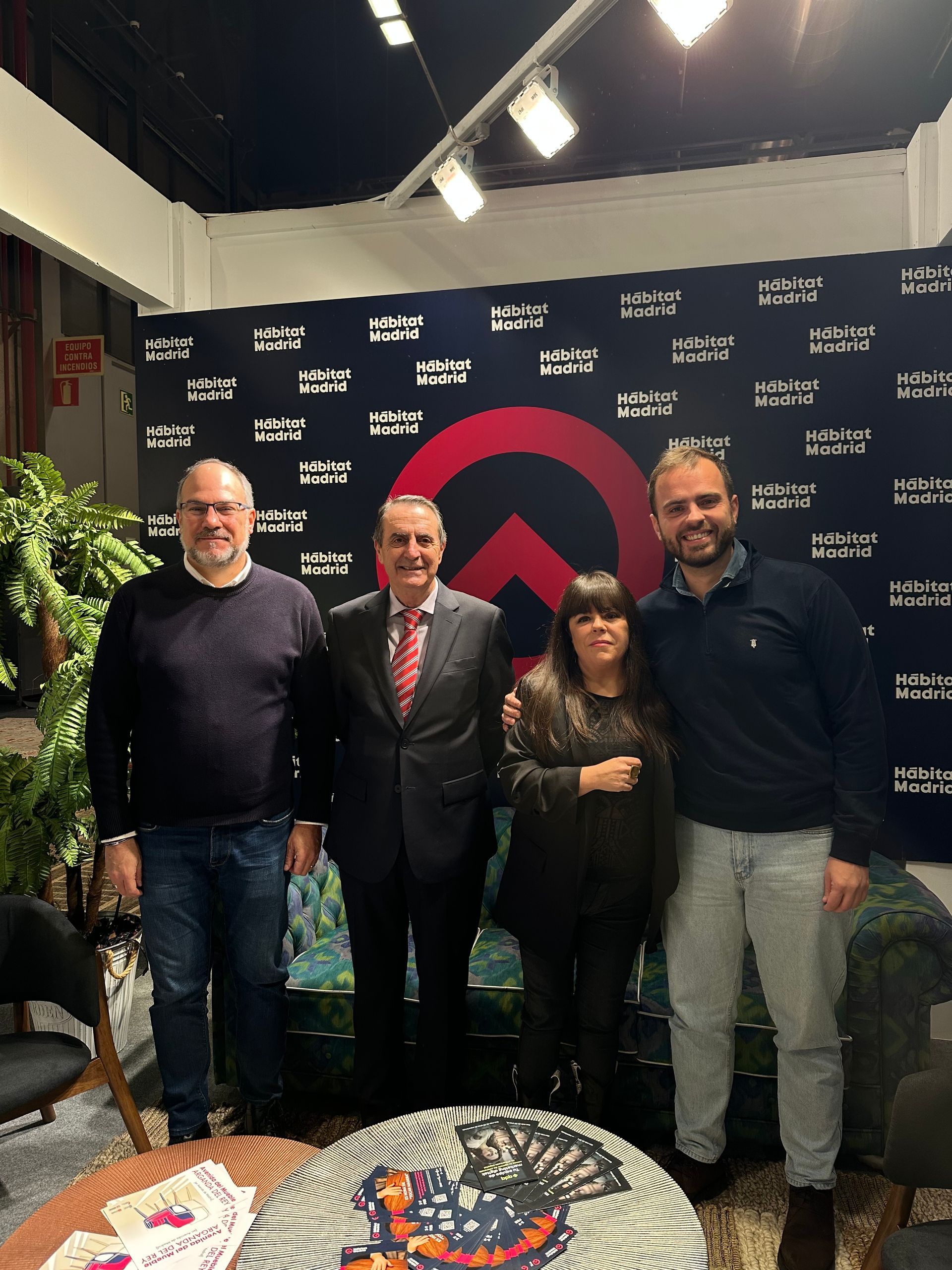 Cuatro personas posando en interiores frente a un fondo con la marca de la empresa, con plantas e iluminación de estudio.