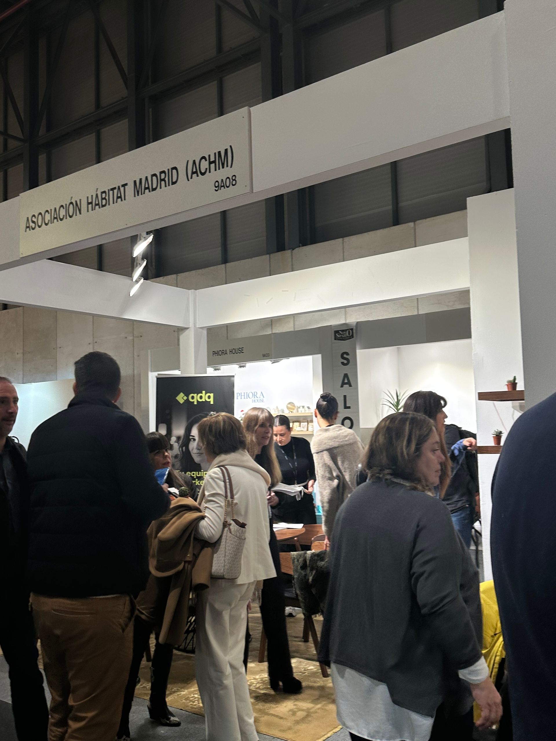 Gente curioseando entre los stands de una concurrida feria cubierta, con un gran letrero blanco sobre ella.