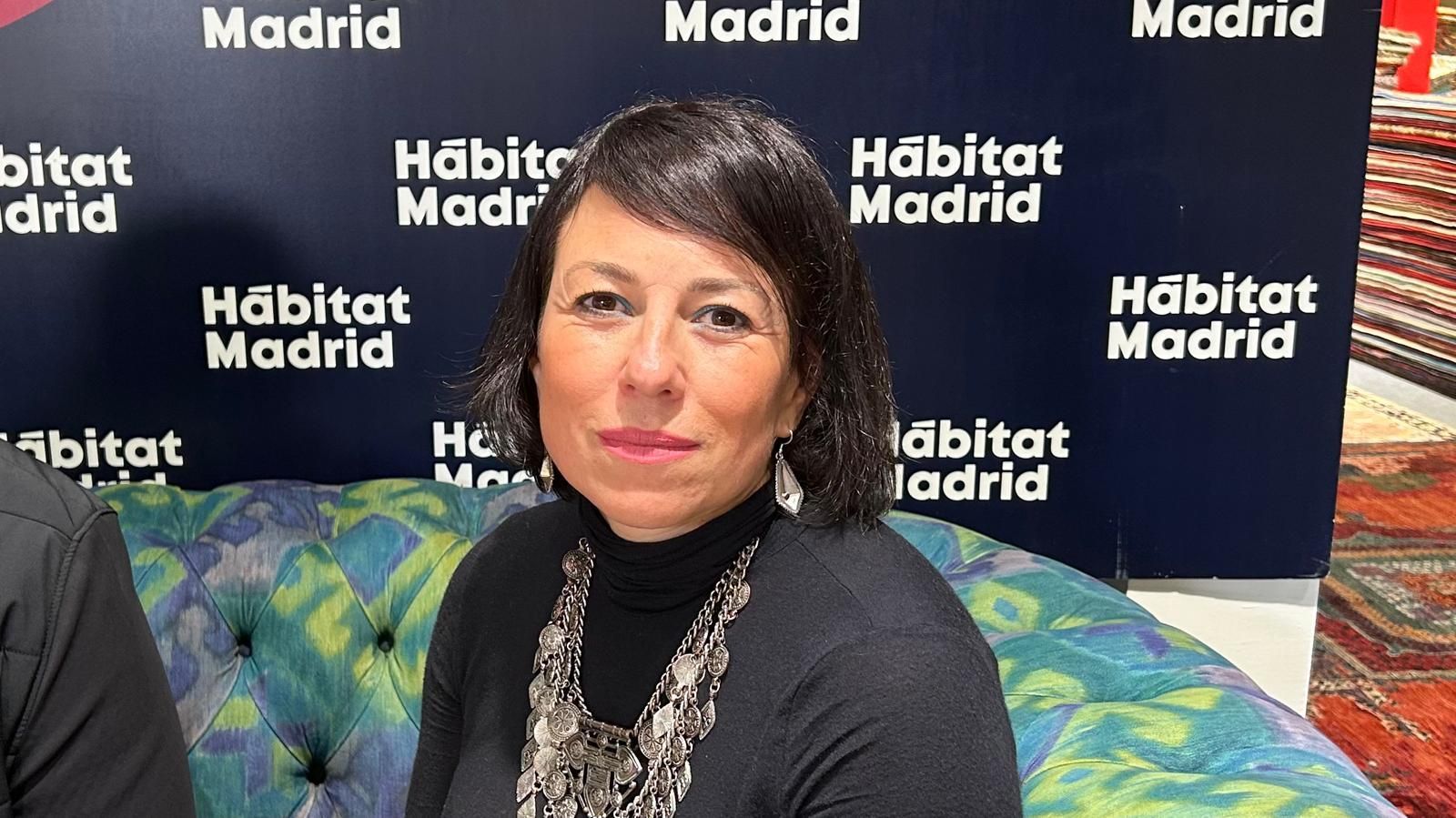 Mujer sentada en un sofá colorido como telón de fondo de un evento de Hábitat Madrid, mirando a la cámara.
