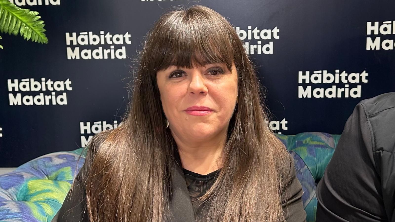 Mujer de pelo largo castaño sentada frente a un telón de fondo con el lema “Hábitat Madrid”