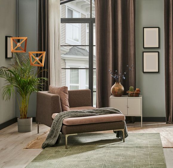 Sala de estar con sillón marrón, alfombra verde, ventana y cortinas marrones.