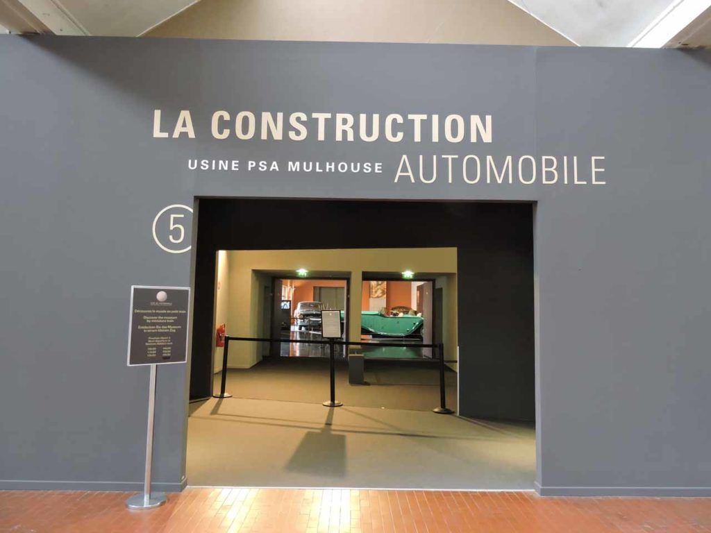 Entrée d'une exposition de musée sur la construction automobile, avec le texte « LA CONSTRUCTION AUTOMOBILE ». Numérotée (5).