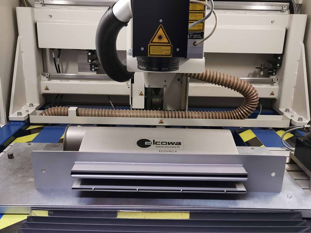 Machine de découpe laser, blanche et argentée, avec tête laser, tubes d'évacuation et surface de travail.