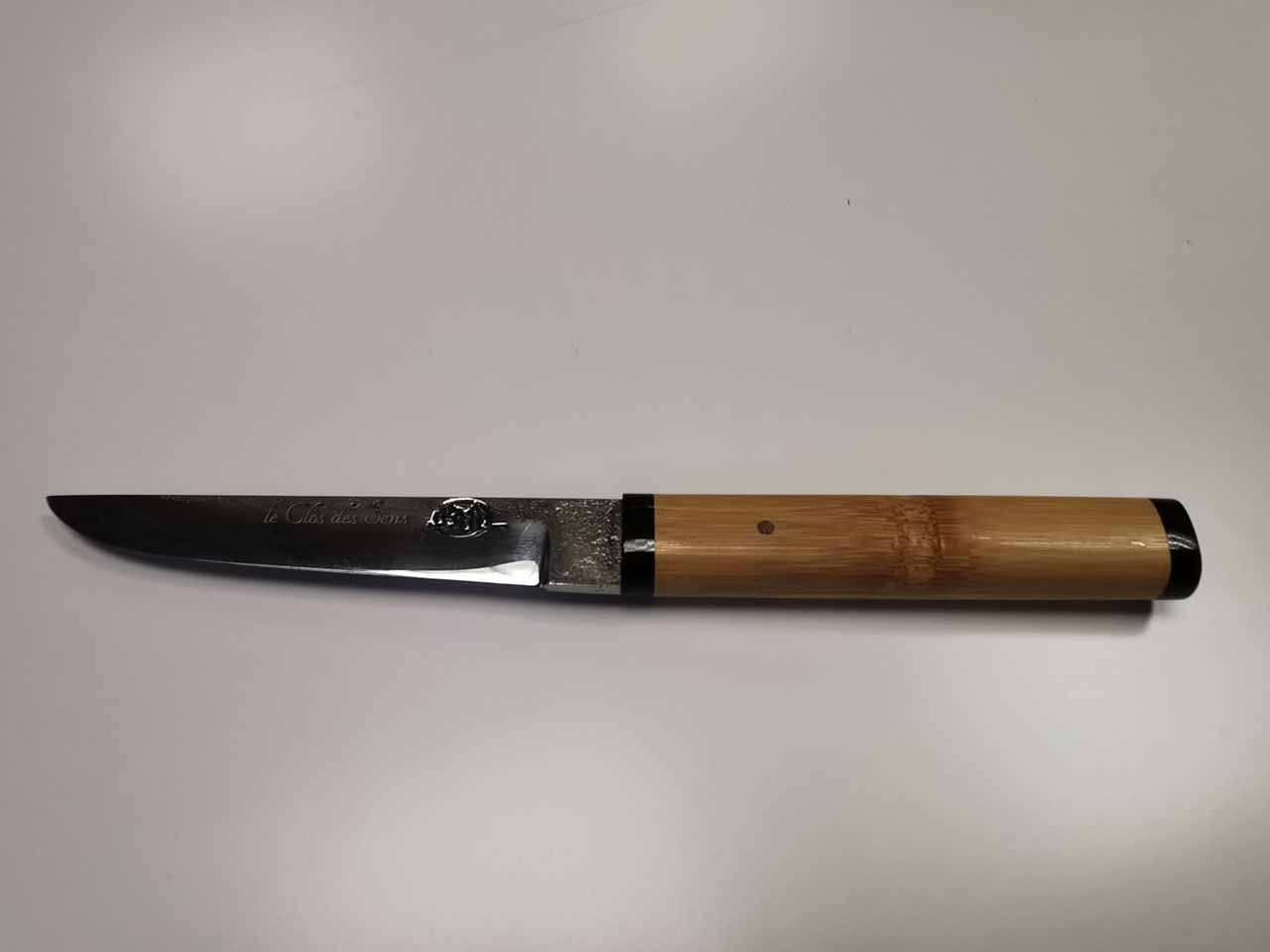 Couteau à manche en bambou sur une surface blanche.