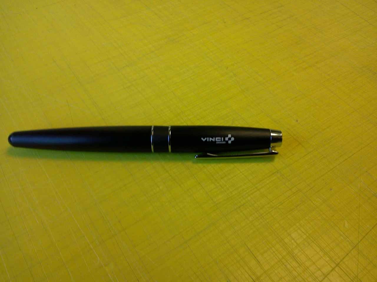 Stylo noir sur fond jaune, avec des détails argentés et un logo près de l'agrafe.