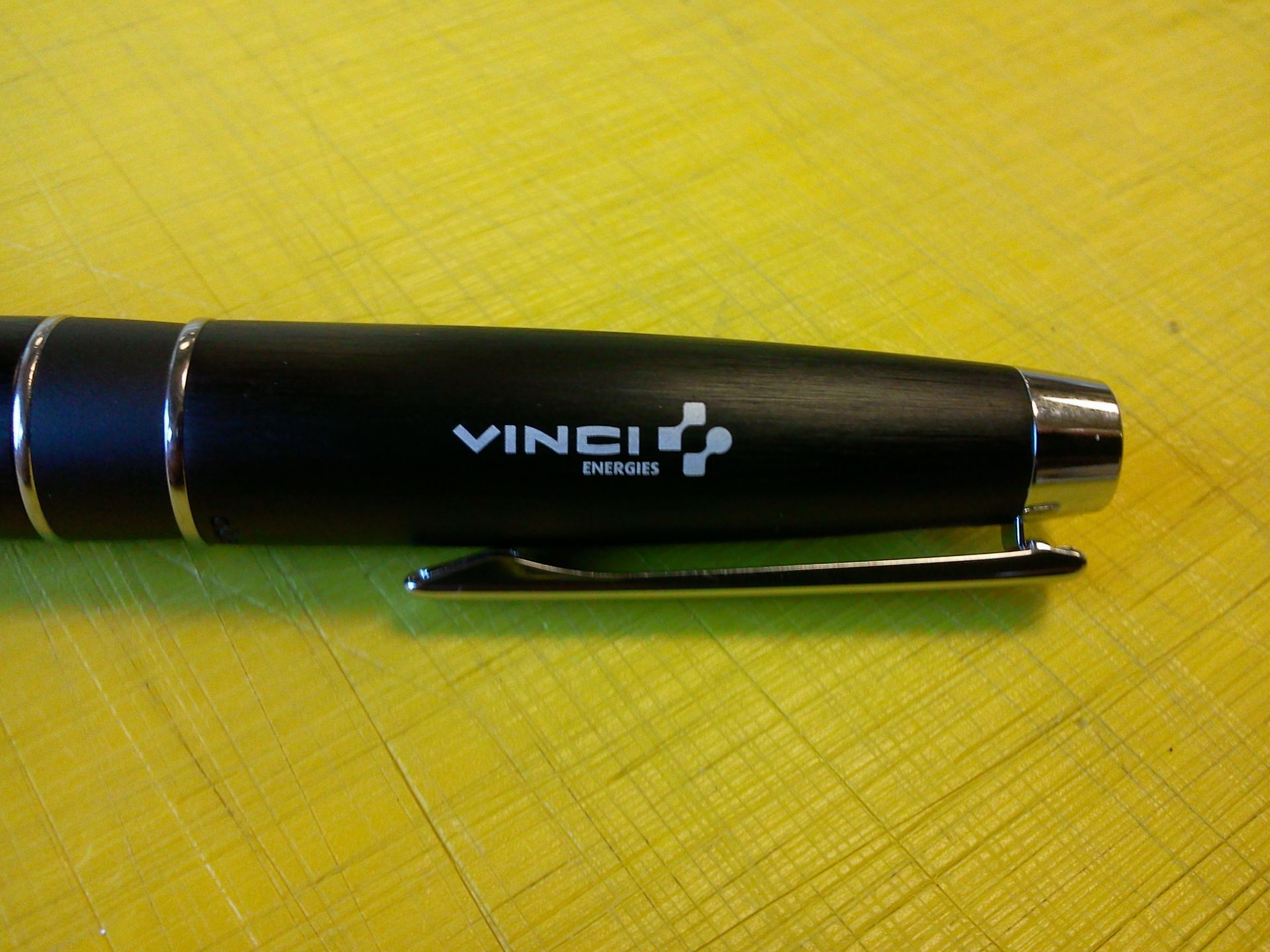 Stylo noir « VINCI » avec détails argentés et clip sur fond jaune.