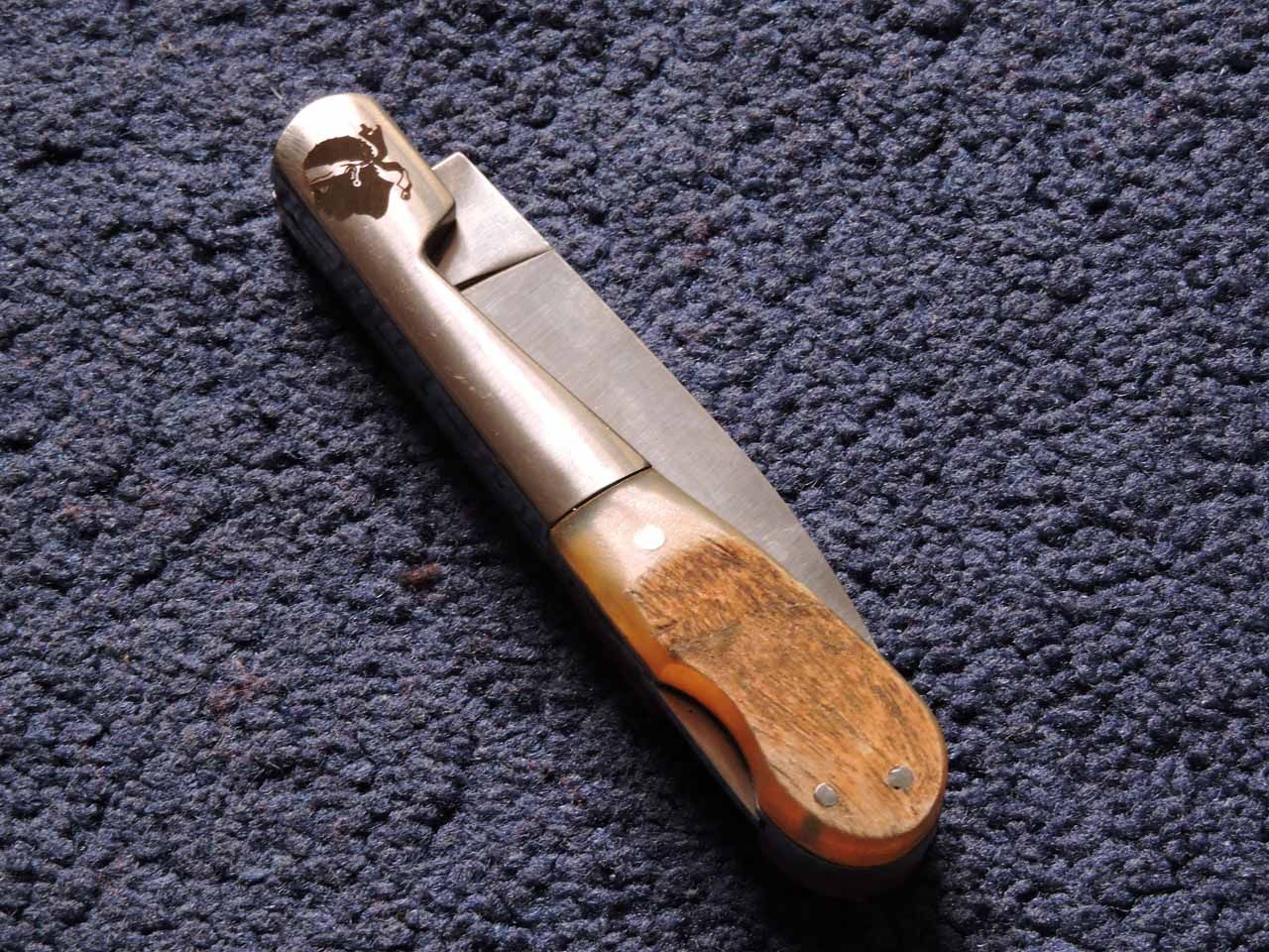 Couteau de poche à manche en bois, partiellement ouvert, sur un tapis bleu.