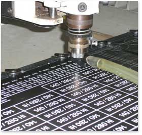 Une machine CNC découpant des étiquettes dans une feuille de matériau noir, le texte « 140/280 HI » visible sur de nombreuses étiquettes.