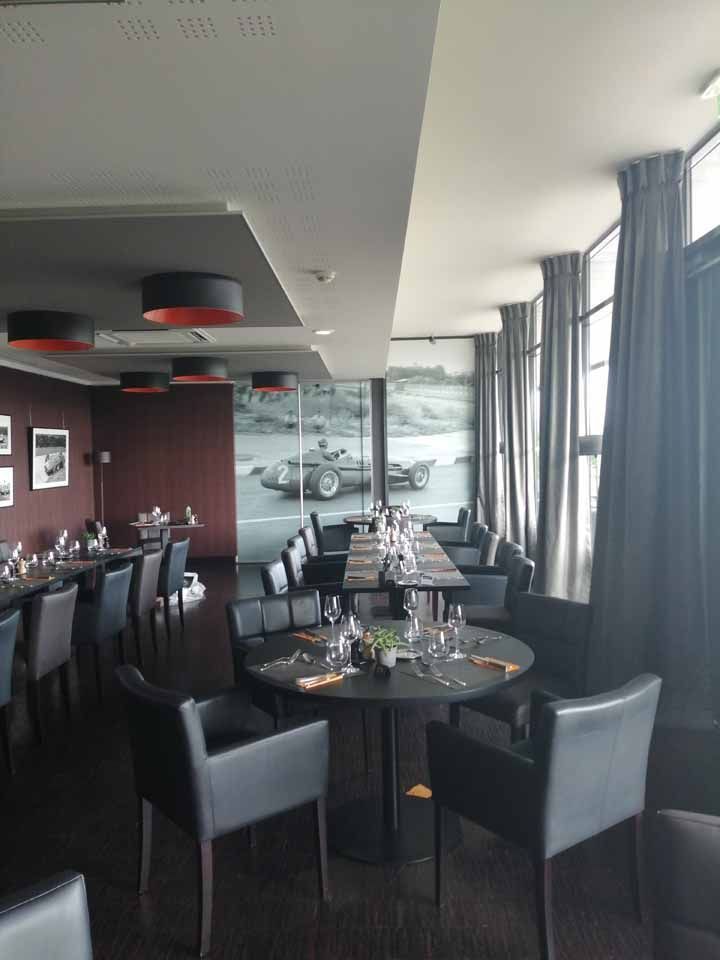 Intérieur de restaurant avec tables et chaises sombres. Fresque murale représentant une voiture de course. Rideaux sombres et touches de rouge.