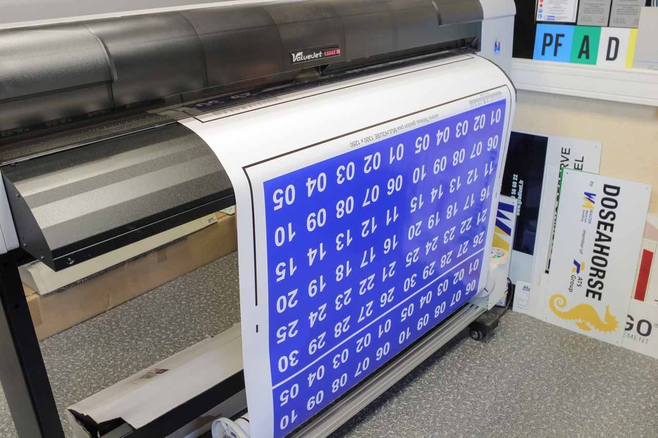 Une imprimante grand format imprimant un panneau bleu et blanc avec des lignes numérotées et du texte.