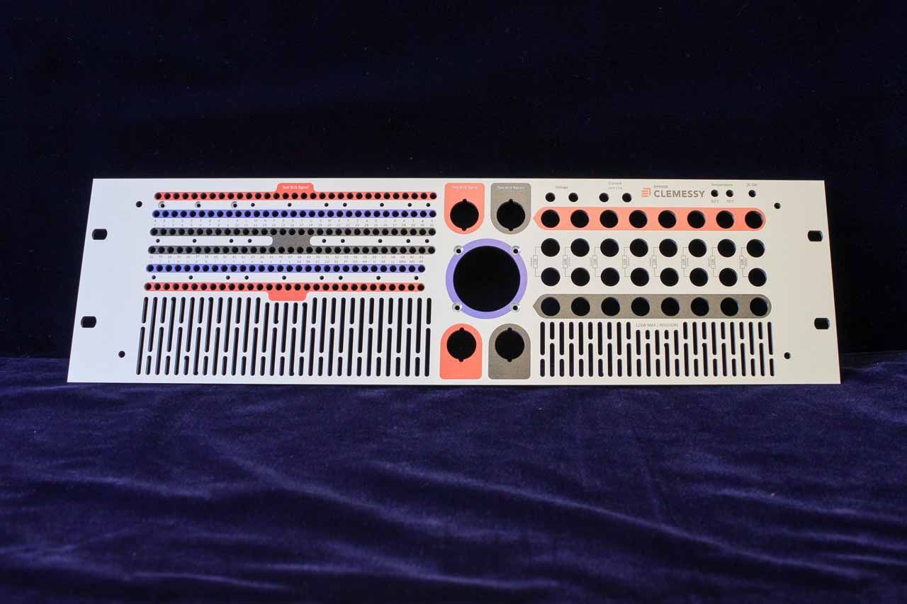 Panneau de rack audio en métal blanc avec divers trous, fentes et marquages colorés sur fond bleu.