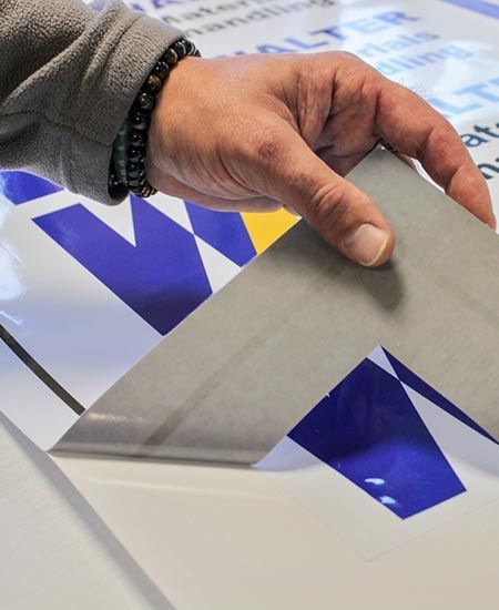 Application manuelle d'un autocollant gris sur un motif bleu et blanc, lui-même placé sur une surface blanche.