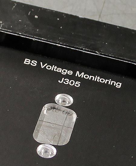 Panneau noir avec le texte « BS Voltage Monitoring J305 » et deux autocollants circulaires transparents au-dessus et en dessous d'un autocollant carré quadrillé.