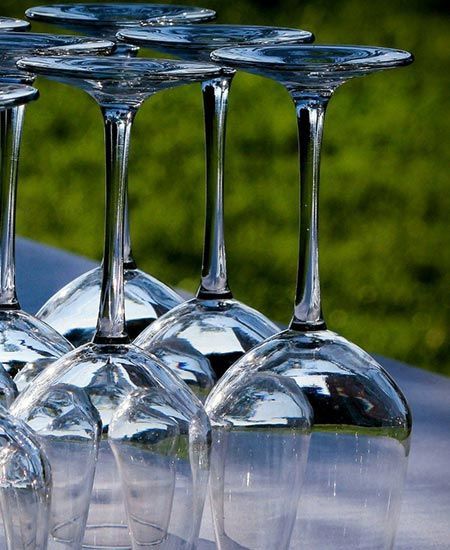 Des verres à vin renversés, alignés sur une table à l'extérieur, avec de l'herbe verte en arrière-plan.