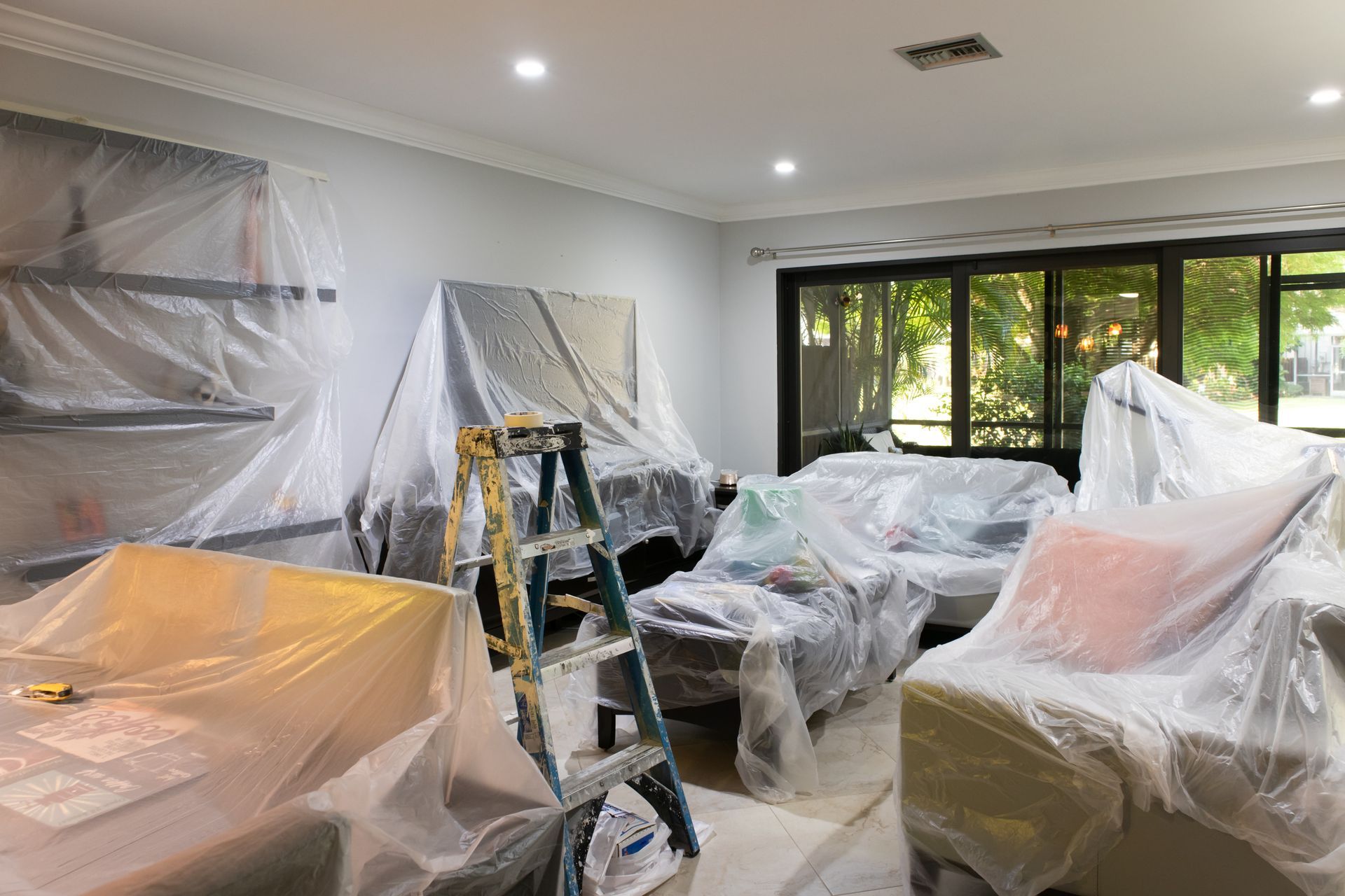 Salon avec meubles couverts de bâches de protection avant travaux de peinture.
