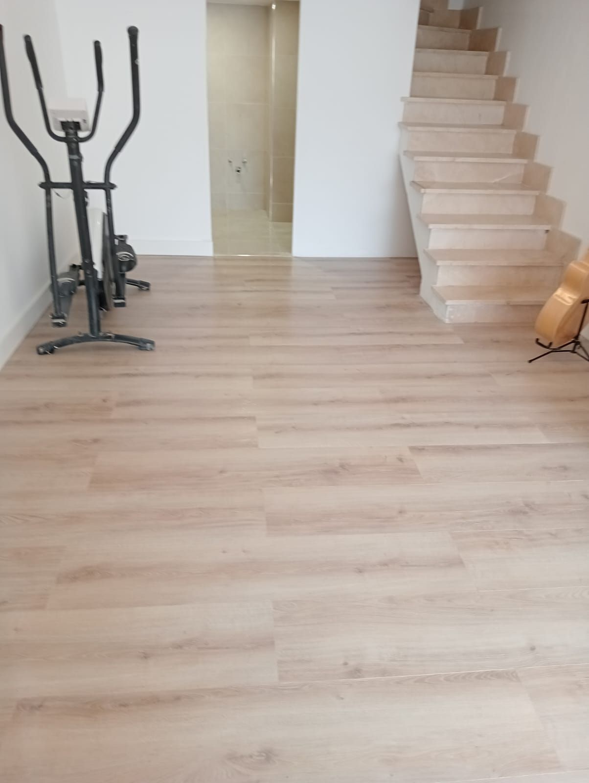 Una habitación con suelo de madera y escaleras y una bicicleta estática.