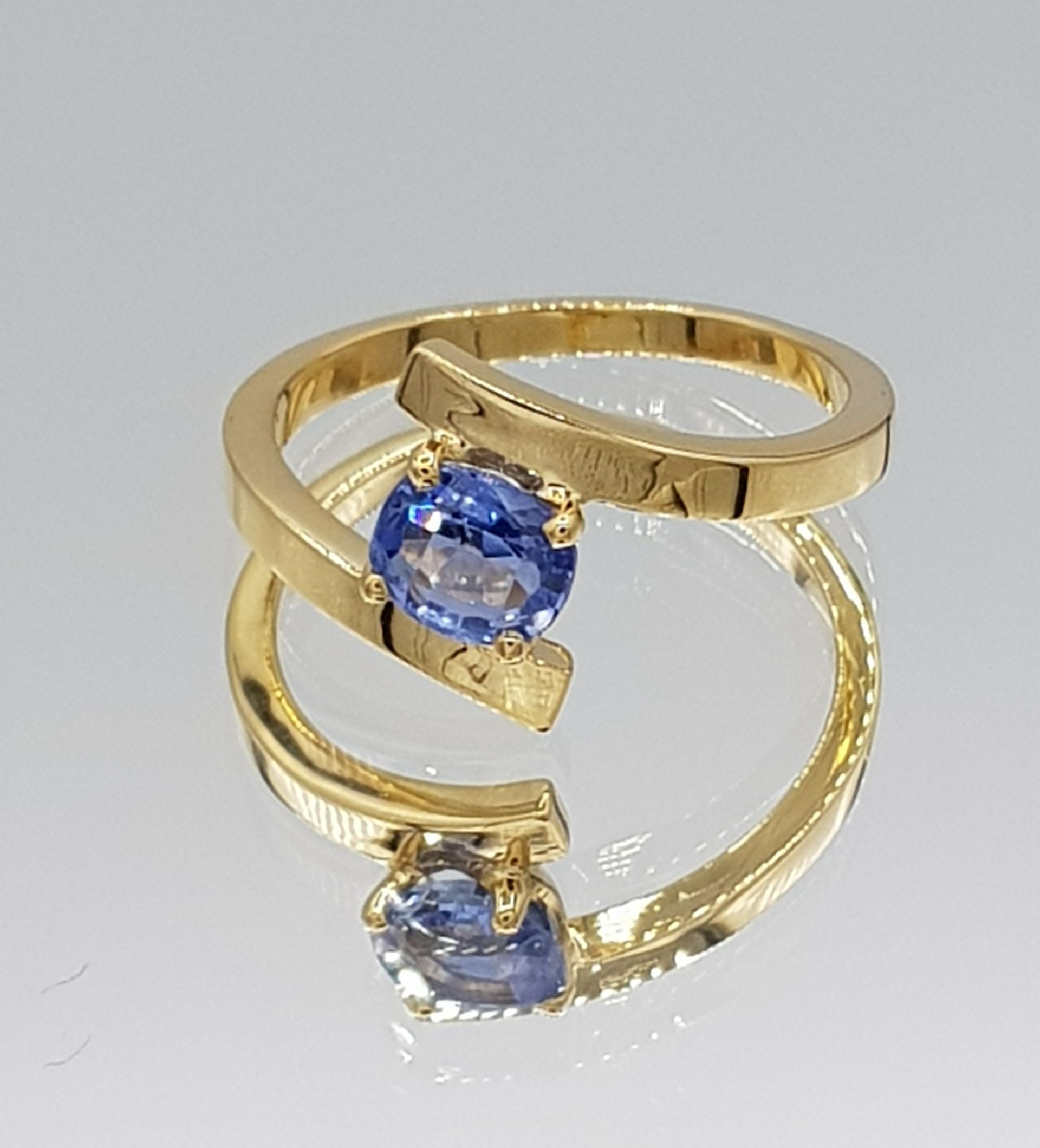 Une bague en or jaune et une pierre bleue posée sur un plateau miroir créée par l'Atelier du Beffroy