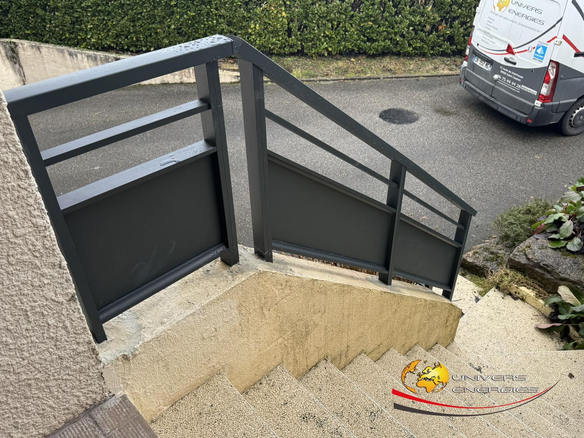 Rambarde métallique grise sur un escalier extérieur, à côté d'un bâtiment et d'un véhicule.