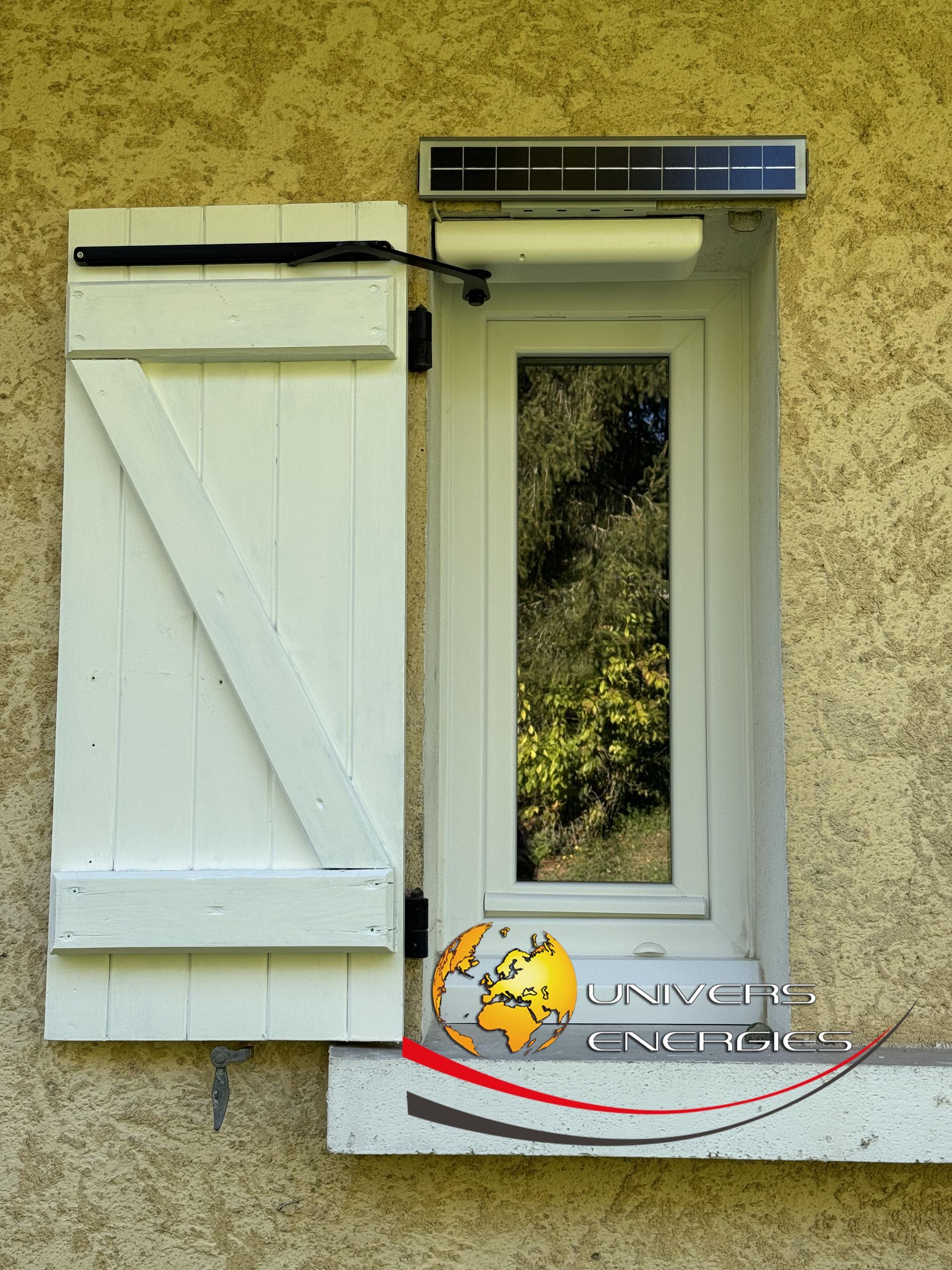 Fenêtre avec volets blancs et ouvre-fenêtre automatique solaire. Mur beige.