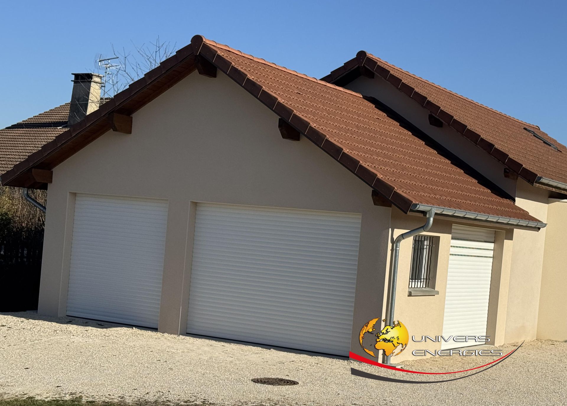 Maison beige avec un toit de tuiles rouges, deux portes de garage et une petite fenêtre.