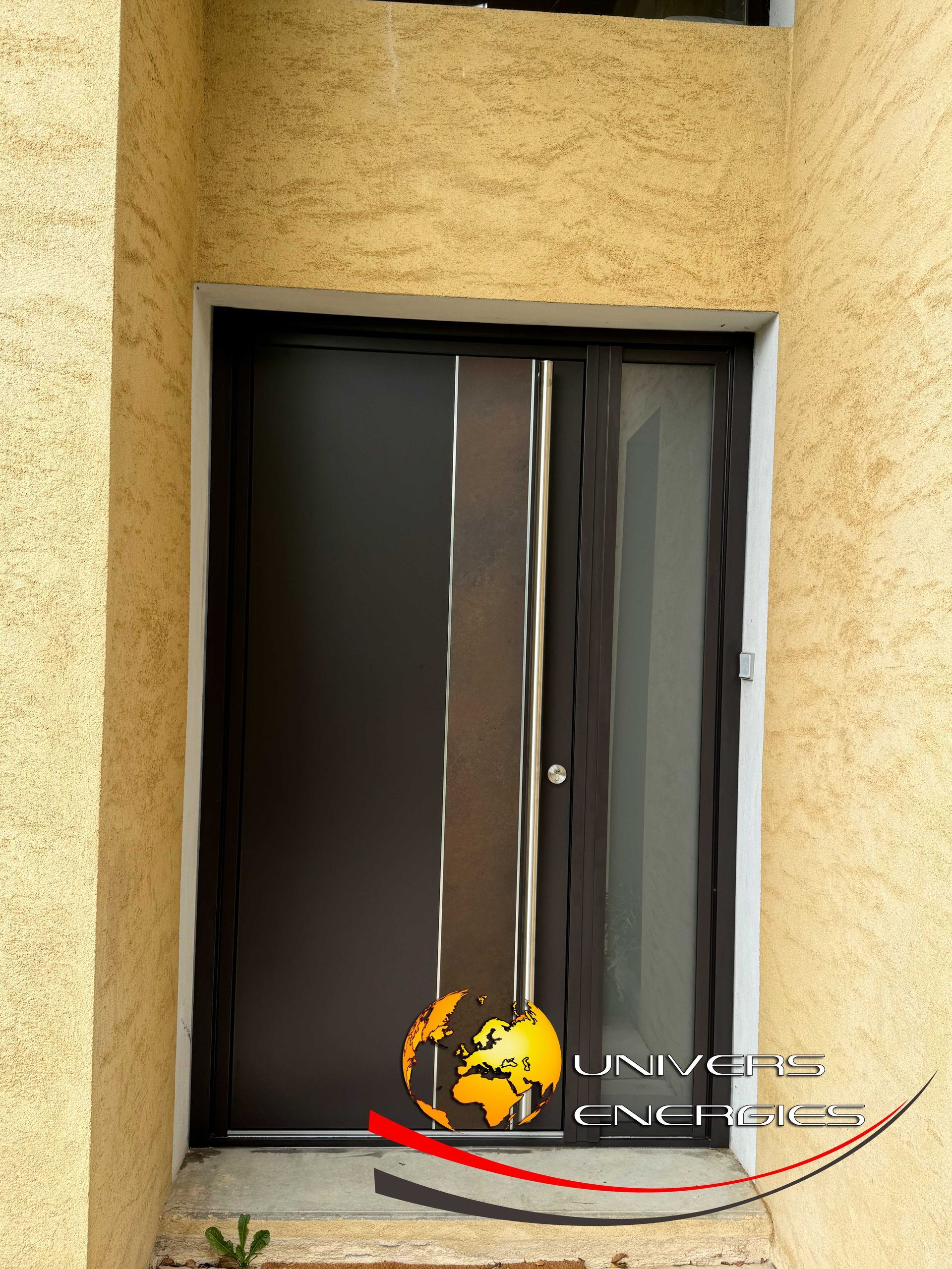 Porte d'entrée brun foncé avec panneau de verre et accents chromés, encastrée dans un mur en stuc beige.