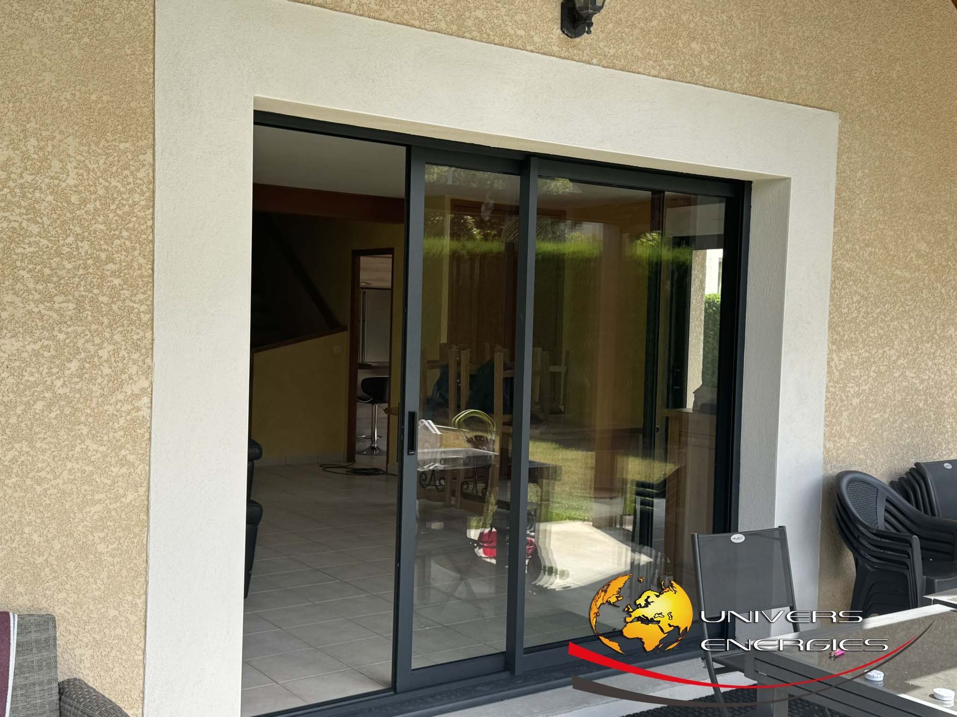 Portes coulissantes en verre à cadre noir sur cadre blanc, donnant sur un intérieur. Vue extérieure avec mobilier de terrasse.