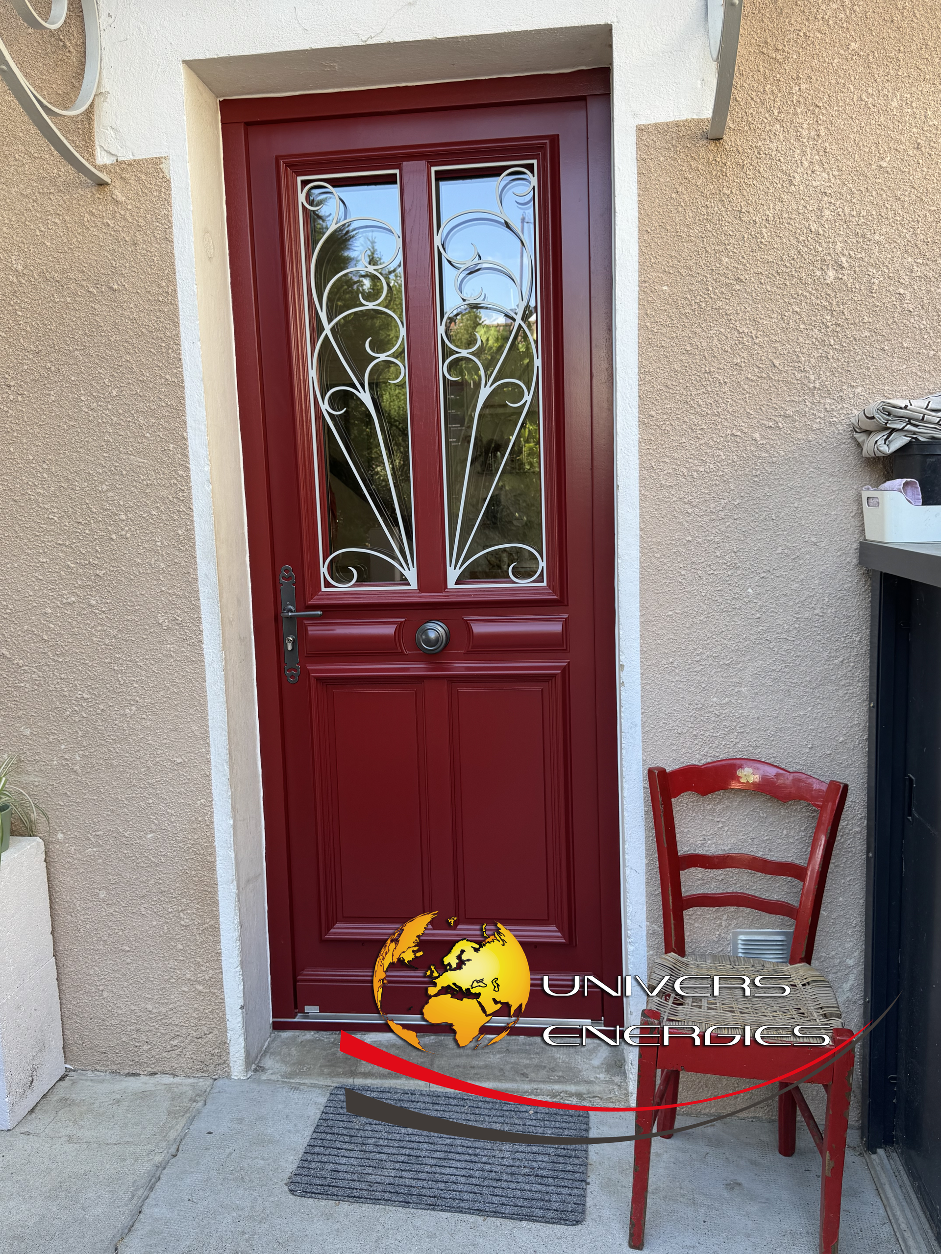 Porte d'entrée rouge avec panneaux de verre, chaise rouge et paillasson sur le porche.