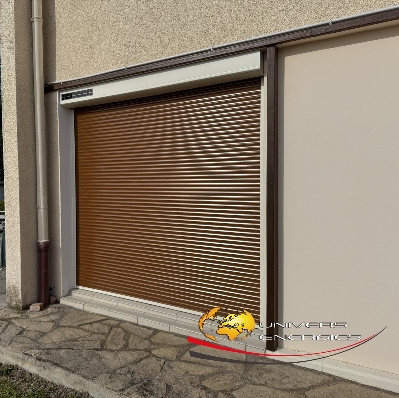 Volet roulant marron fermé sur la façade d'un bâtiment, mur beige, sol en pierre.