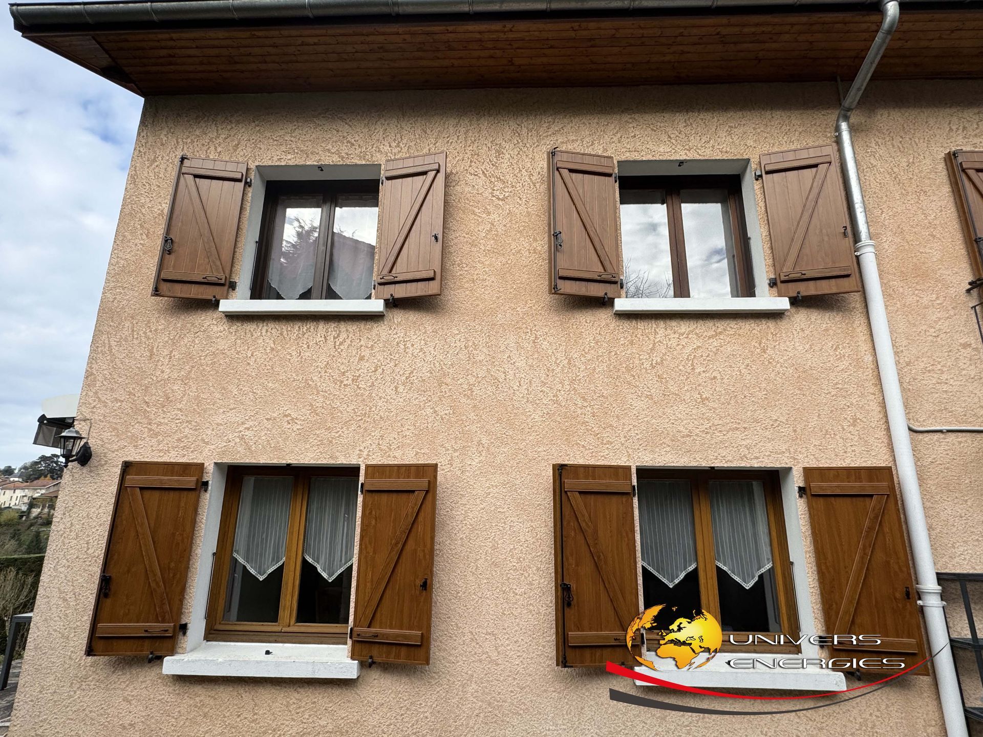 Bâtiment de deux étages avec volets et fenêtres marron. Façade en stuc beige.