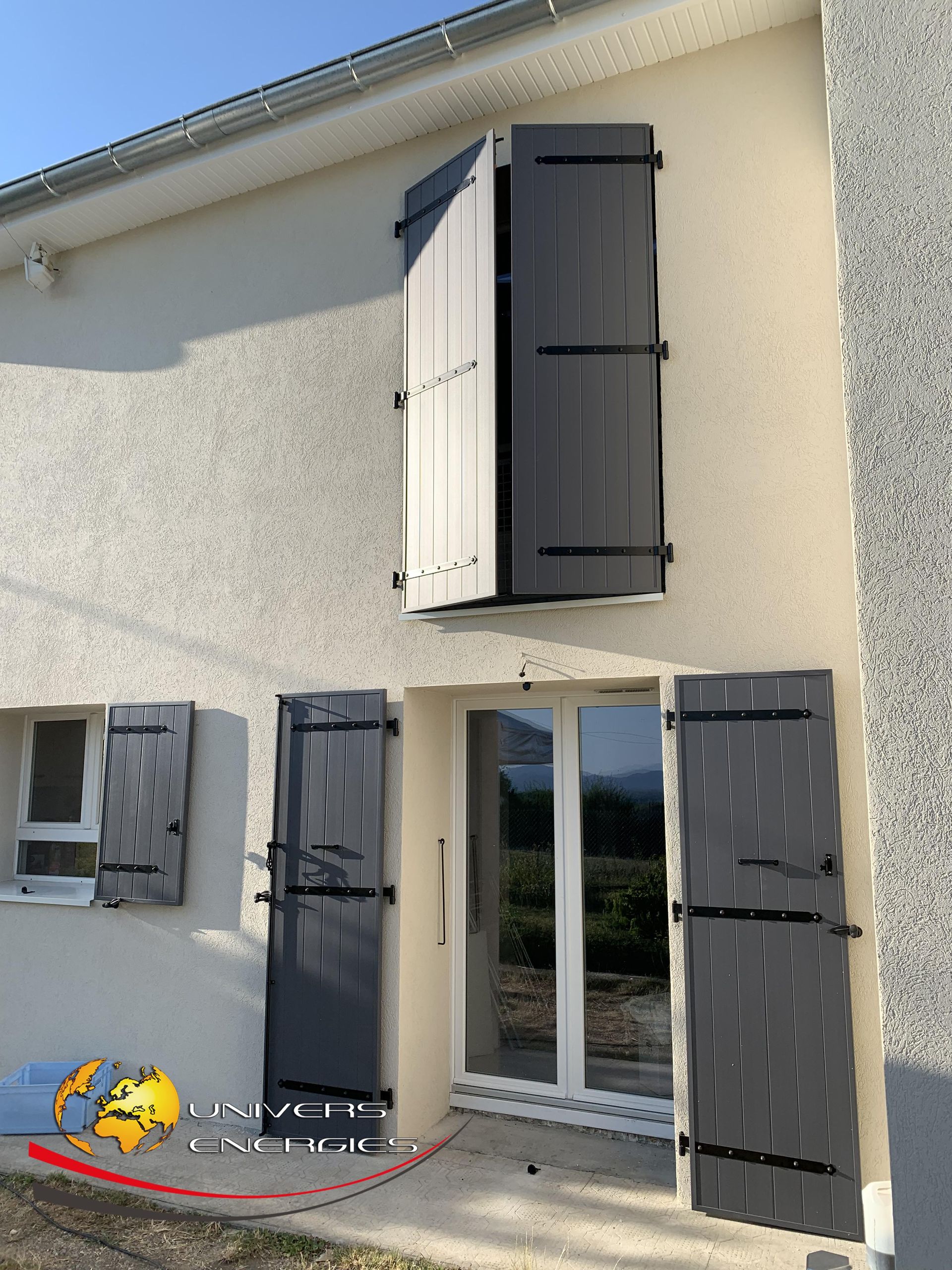 Extérieur d'une maison avec des volets gris. Les volets des fenêtres sont ouverts et fermés.