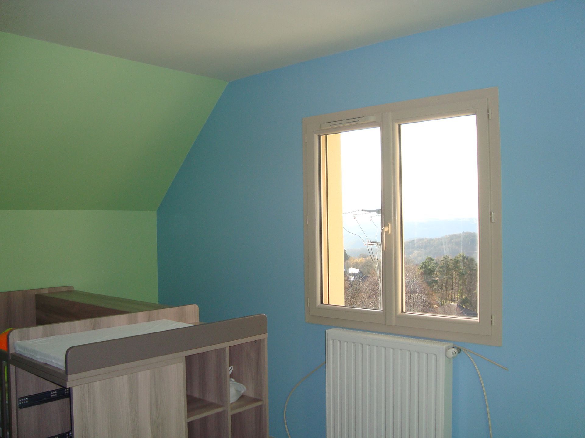 Mur avec fenêtre peint en bleu ciel à côté d'un mur peint en vert clair
