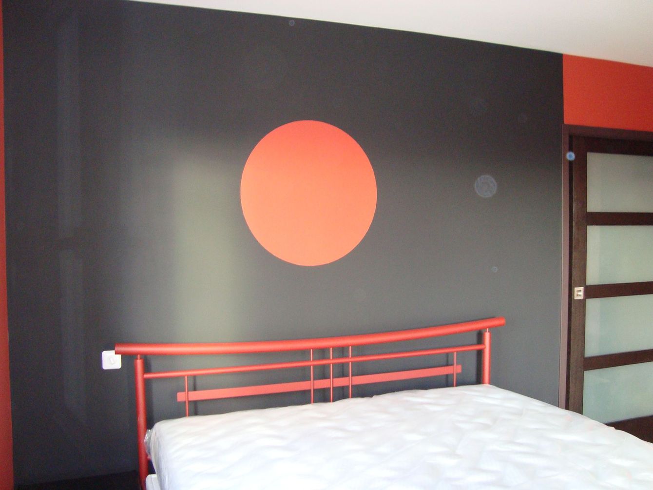 Mur de chambre peint en noir avec un cercle orange au centre, tête de lit d'inspiration asiatique