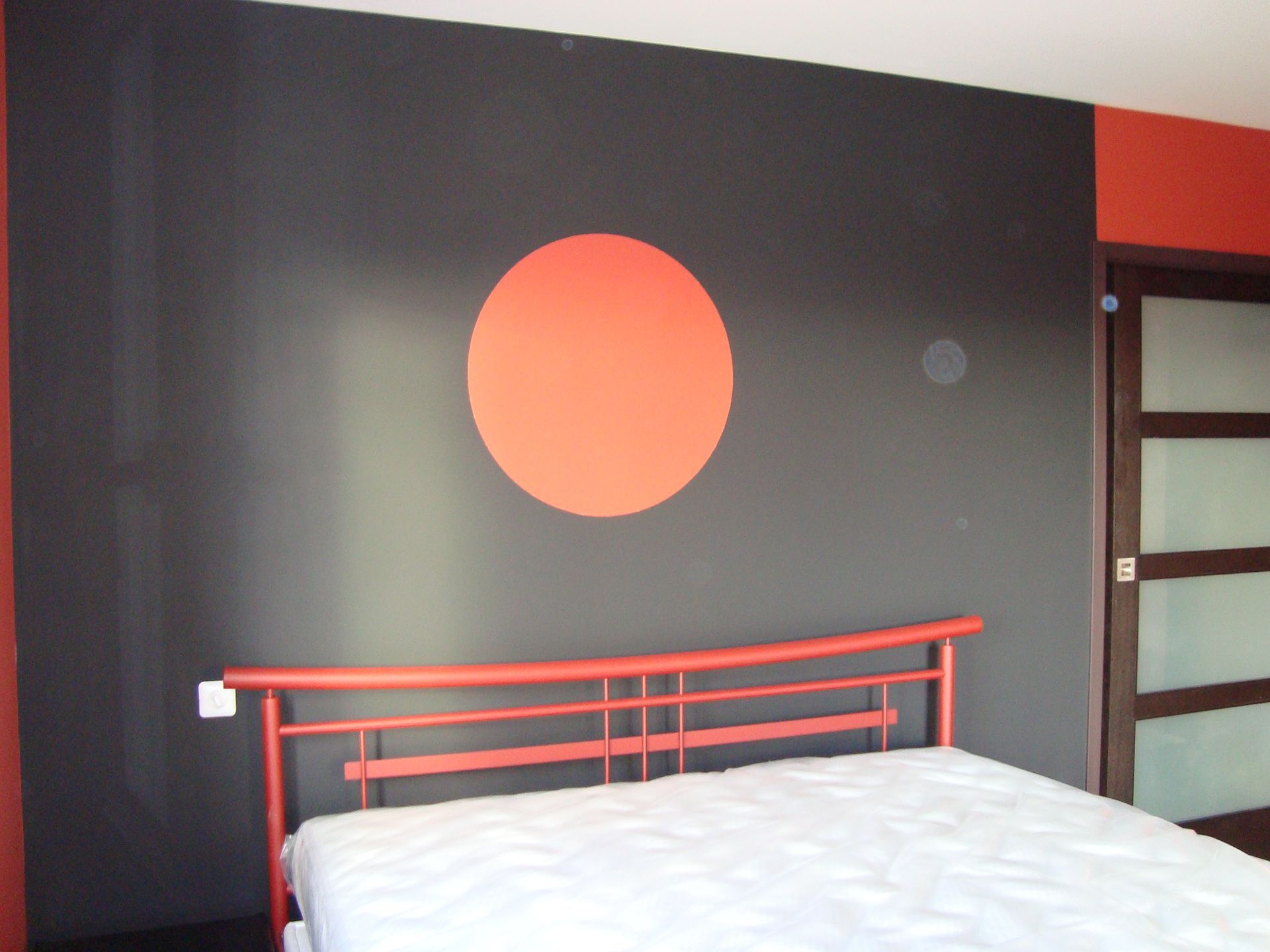 Mur peint en noir, cercle peint en rouge et tête de lit rouge