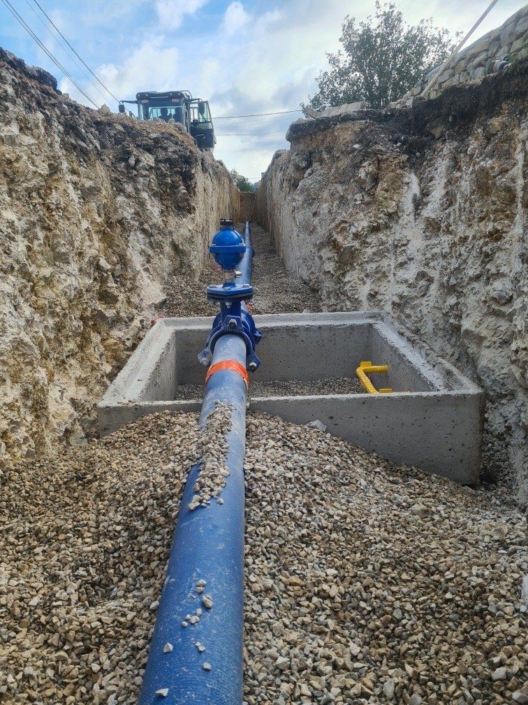 Tuyau d'eau bleu dans une tranchée avec vanne et gravier, carré en béton, ciel bleu, chantier de construction.