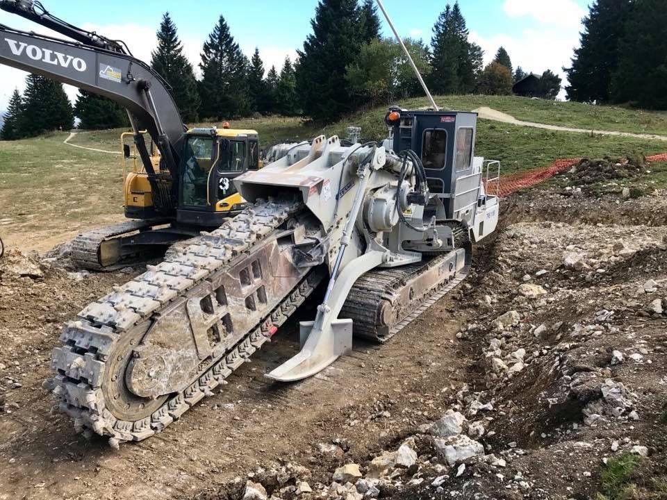 Une trancheuse creusant un trou dans la terre près d'une excavatrice Volvo ; un chantier de construction.