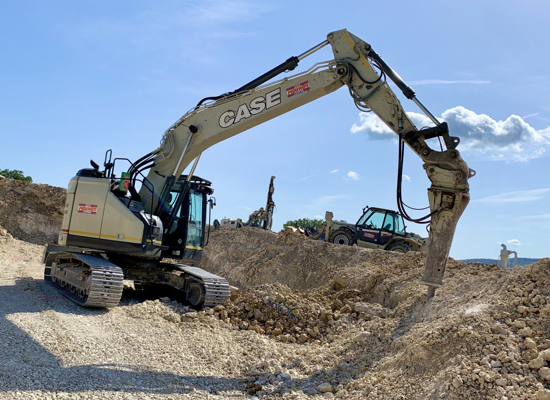 Une excavatrice brise des roches sur un chantier de construction sous un ciel bleu vif.