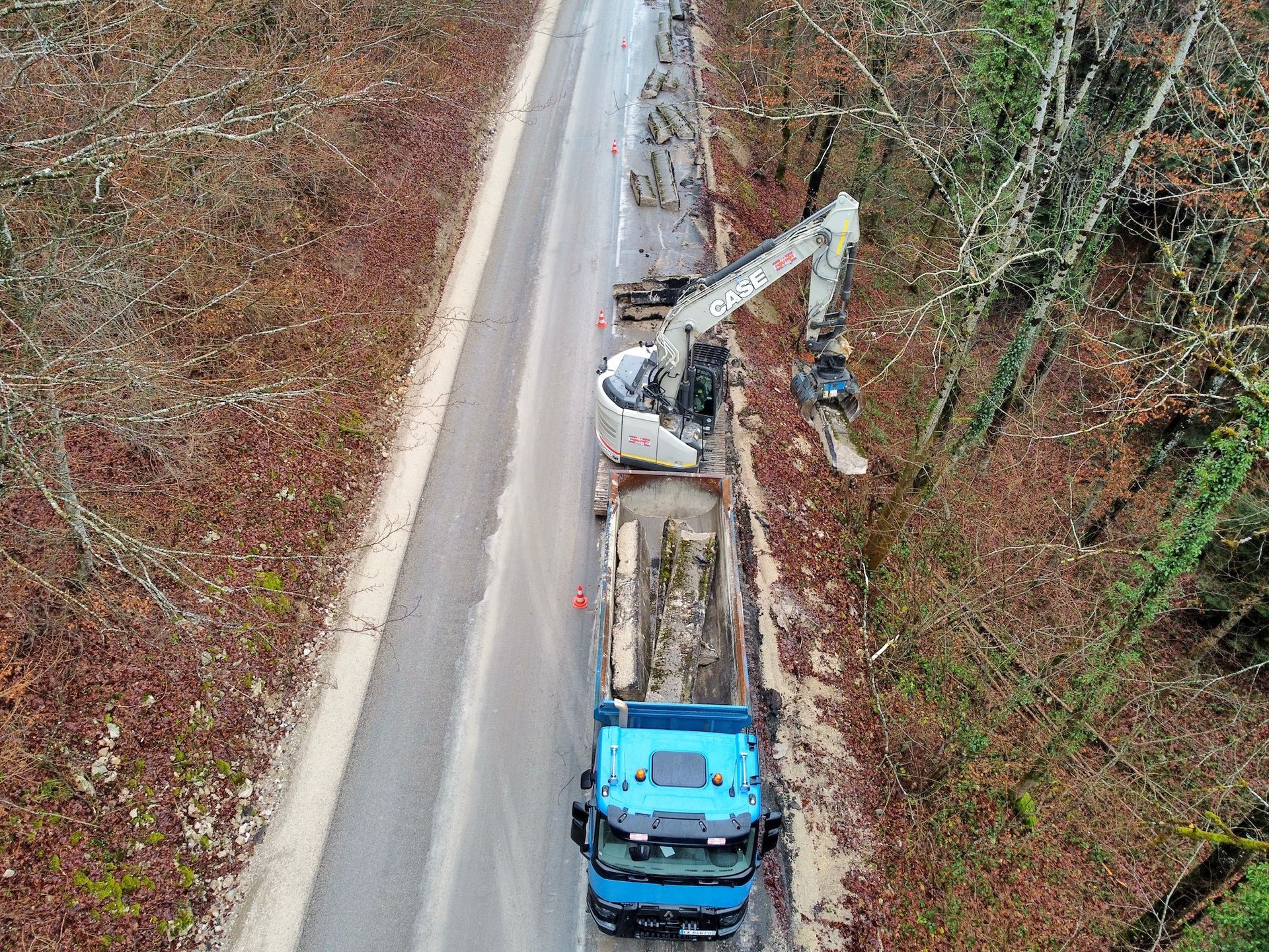 Camion avec excavatrice enlevant des matériaux le long d'une route dans une forêt.