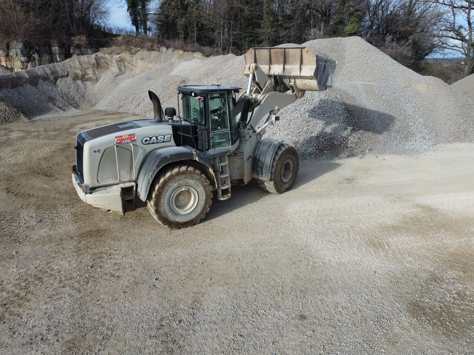 Chargeuse sur pneus récupérant du gravier dans une carrière, avec des tas de gravier en arrière-plan.