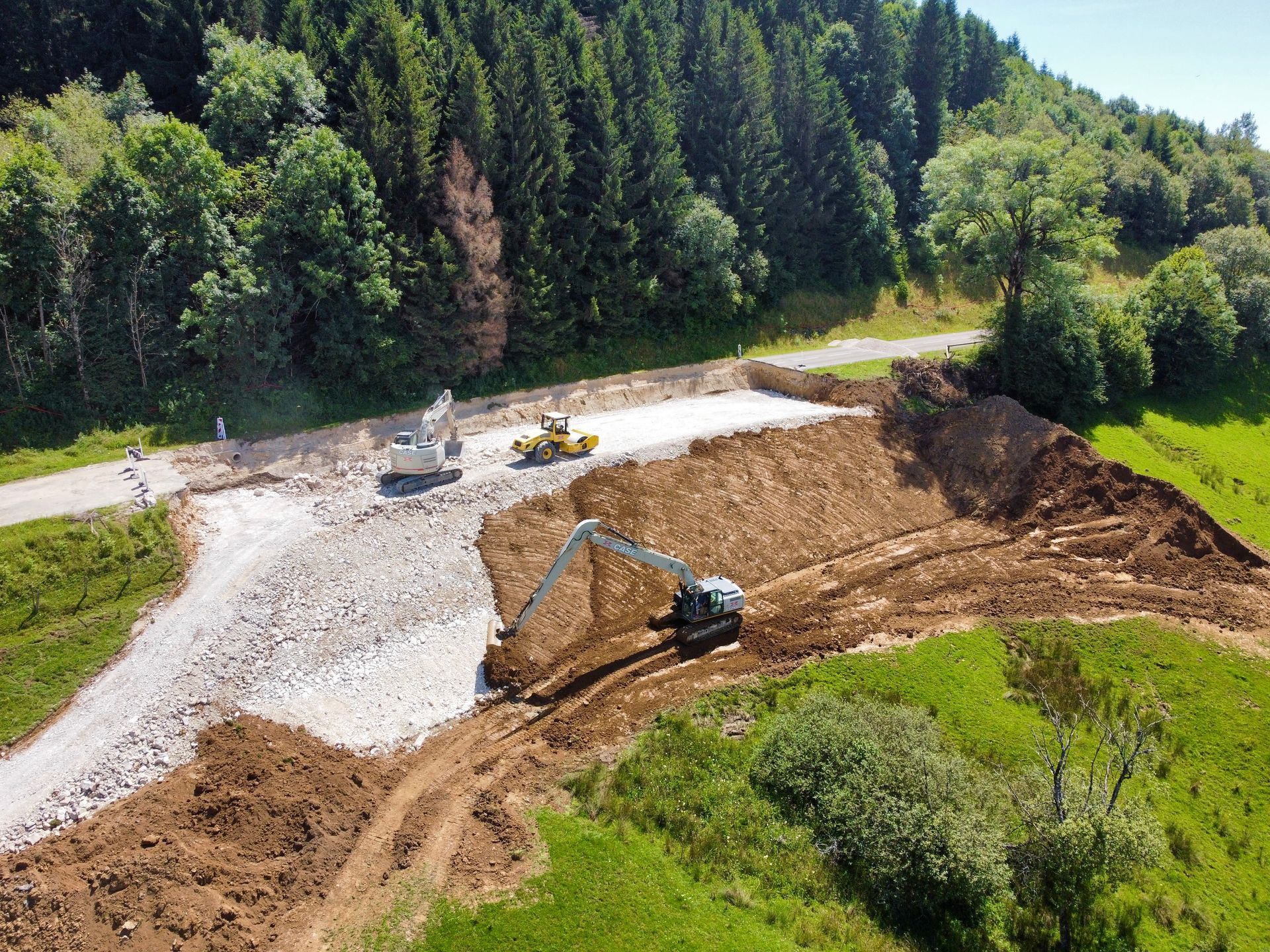 Chantier de construction : Des excavatrices construisent une route à travers une colline verdoyante avec des arbres.