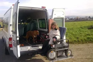 Rollstuhlfahrerin vor einem offenen Kofferraum eines Vans