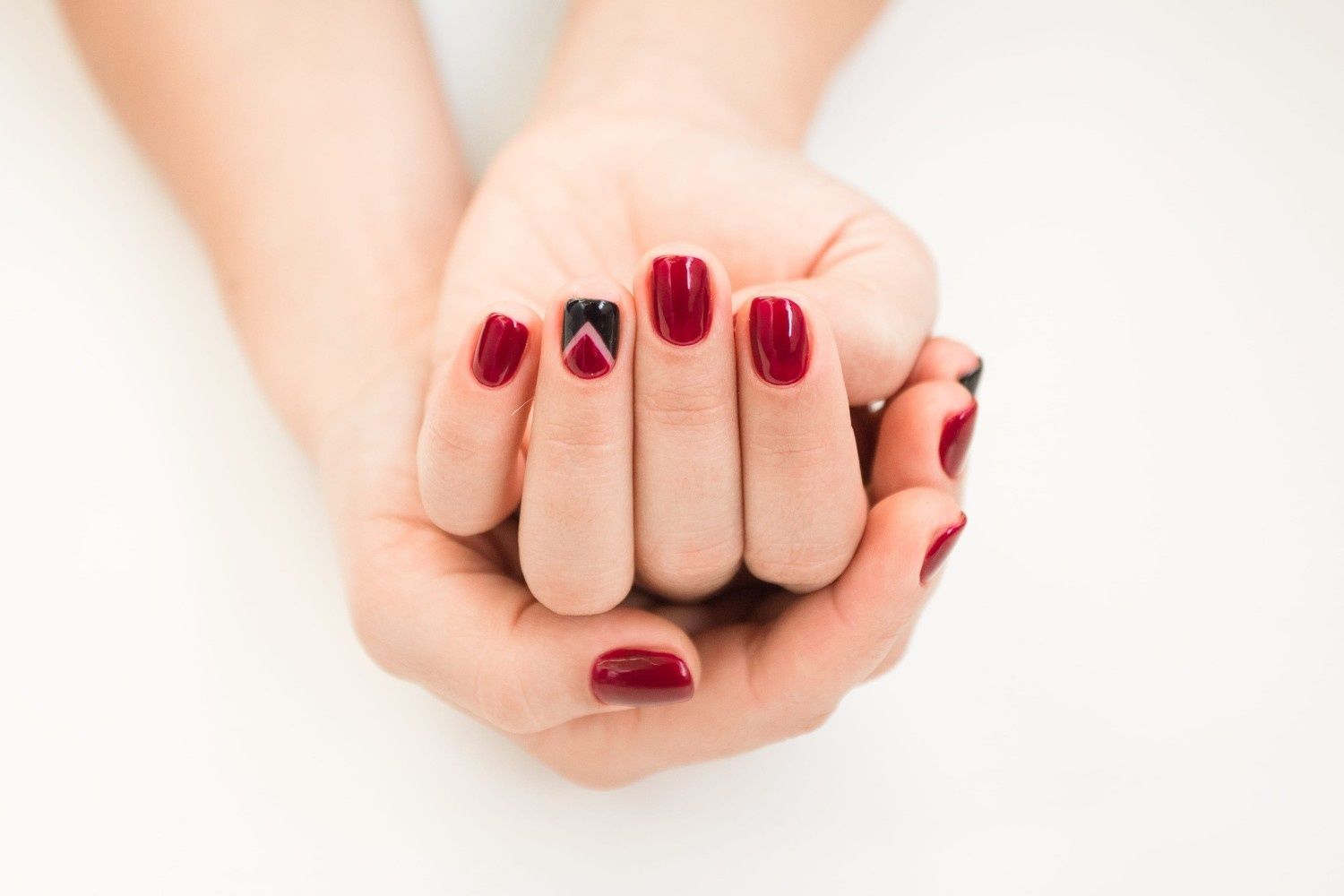 Manos con manicura de color rojo intenso, un puño cerrado sobre el otro sobre un fondo blanco.