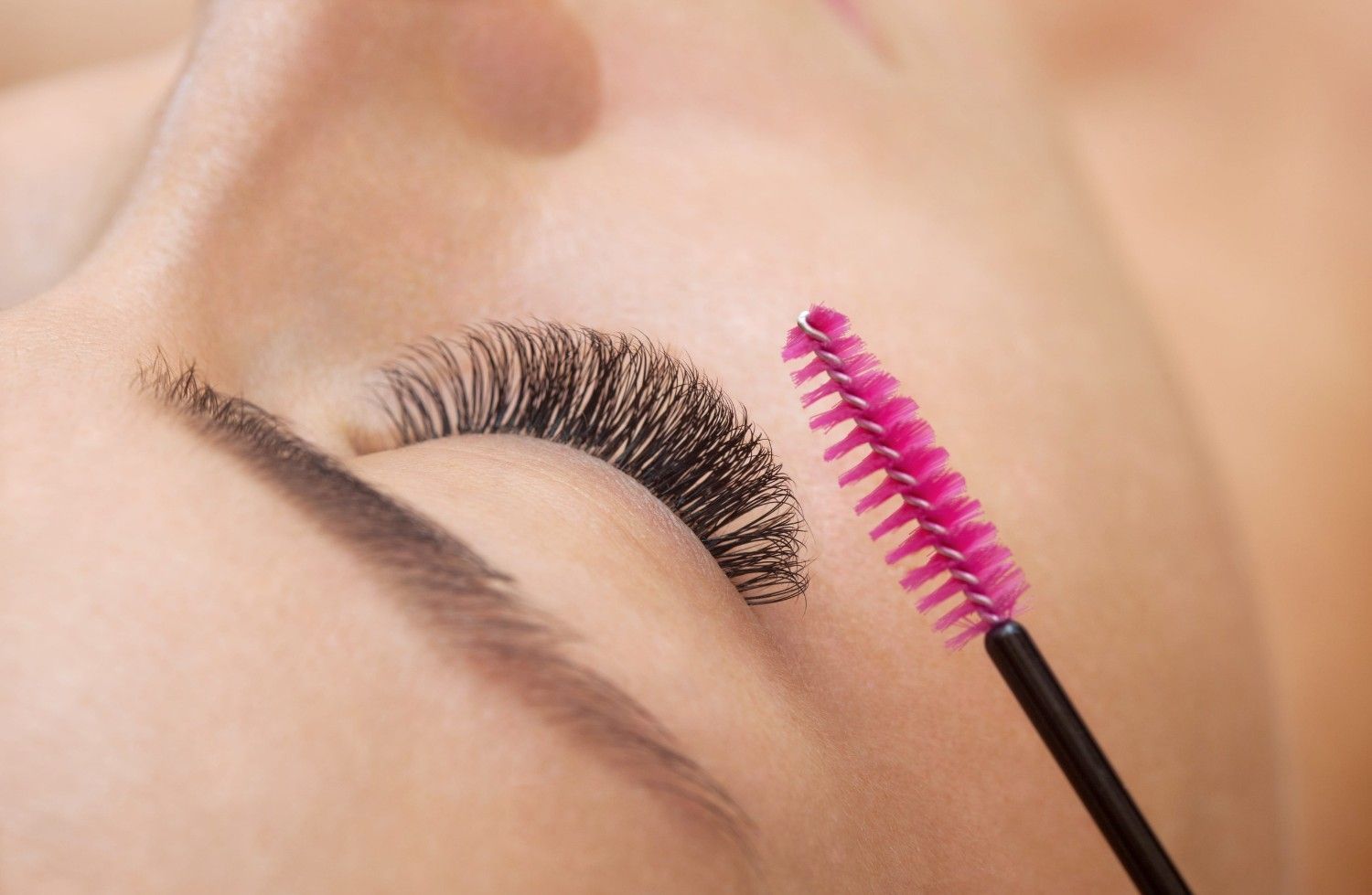 Cepillo para extensiones de pestañas peinando un ojo cerrado con pestañas tupidas.