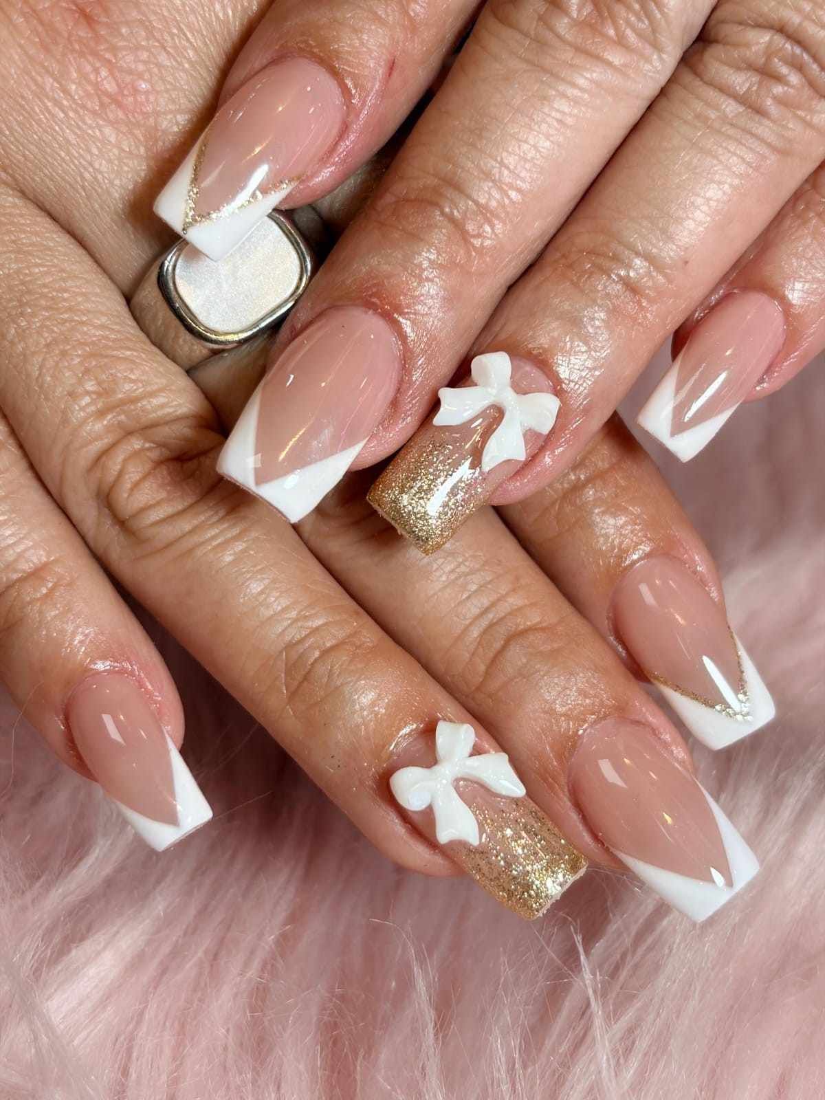 Primer plano de manos bien cuidadas con uñas pintadas en tonos nude, blanco y dorado, con punta francesa y detalles de lazos.