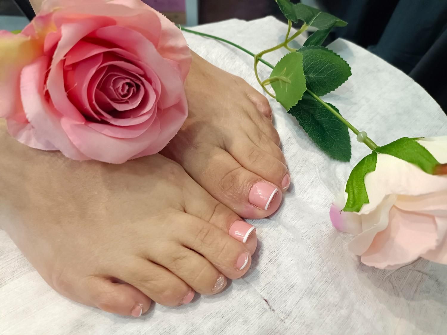 Pies con uñas pintadas de rosa junto a rosas rosas sobre una toalla blanca.