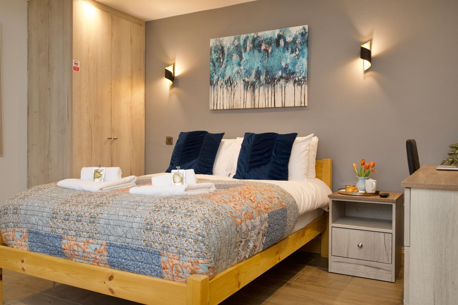 Cozy hotel room with a queen bed, blue accents, bedside table, and wall art